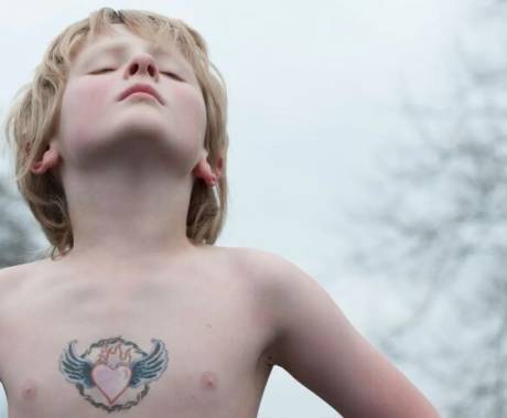 dítě s tetováním srdce s křídly stojící v pozoru