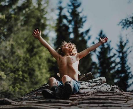 chlapec sedí na kládě stromu s rukama k obloze ve větru