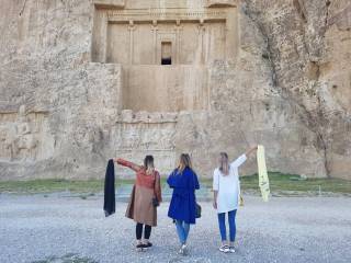 tři ženy před skalním chrámem, dvě mávají šátky