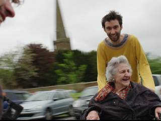 muž veze starou ženu na vozíku, oba se smějí