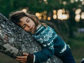 dívka se zavřenýma očima se opírá o kmen stromu