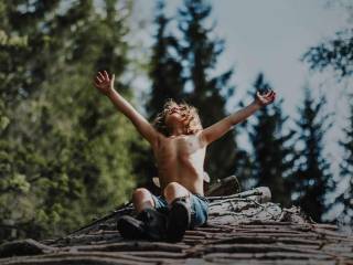 chlapec sedí na kládě stromu s rukama k obloze ve větru