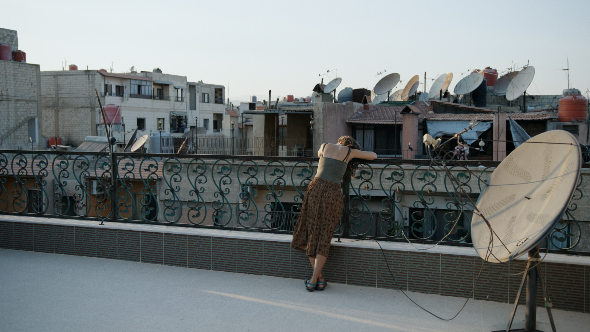 žena opírající se o zábradlí na terase, v pozadí domy