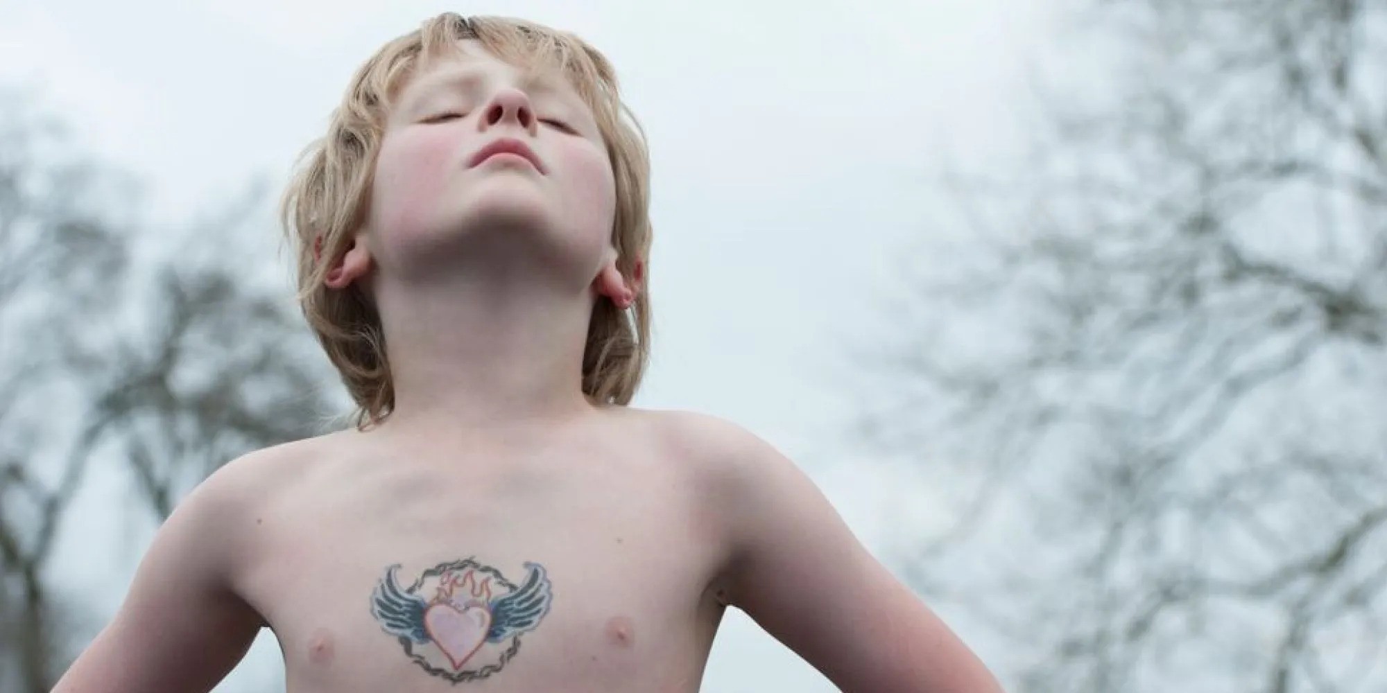 dítě s tetováním srdce s křídly stojící v pozoru